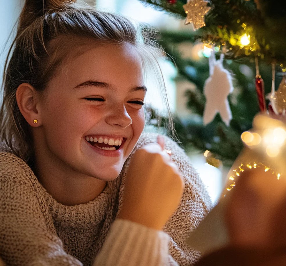 Mädchen lacht am Weihnachtsbaum und trägt goldenen Stern-Ohrstecker aus dem Adventskalender