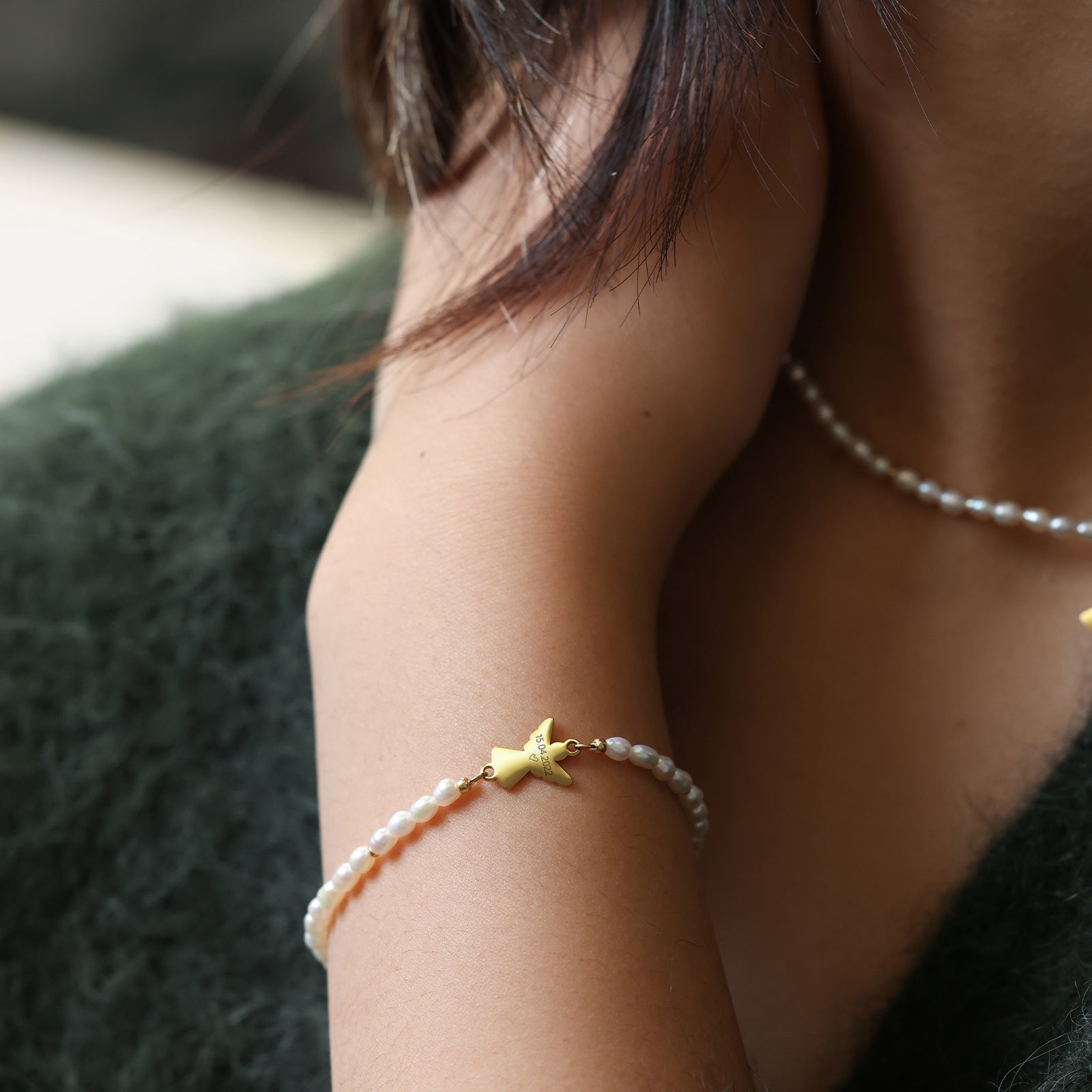 Frau trägt Schutzengel-Perlenarmband am Arm, im Hintergrund eine Perlenkette am Hals
