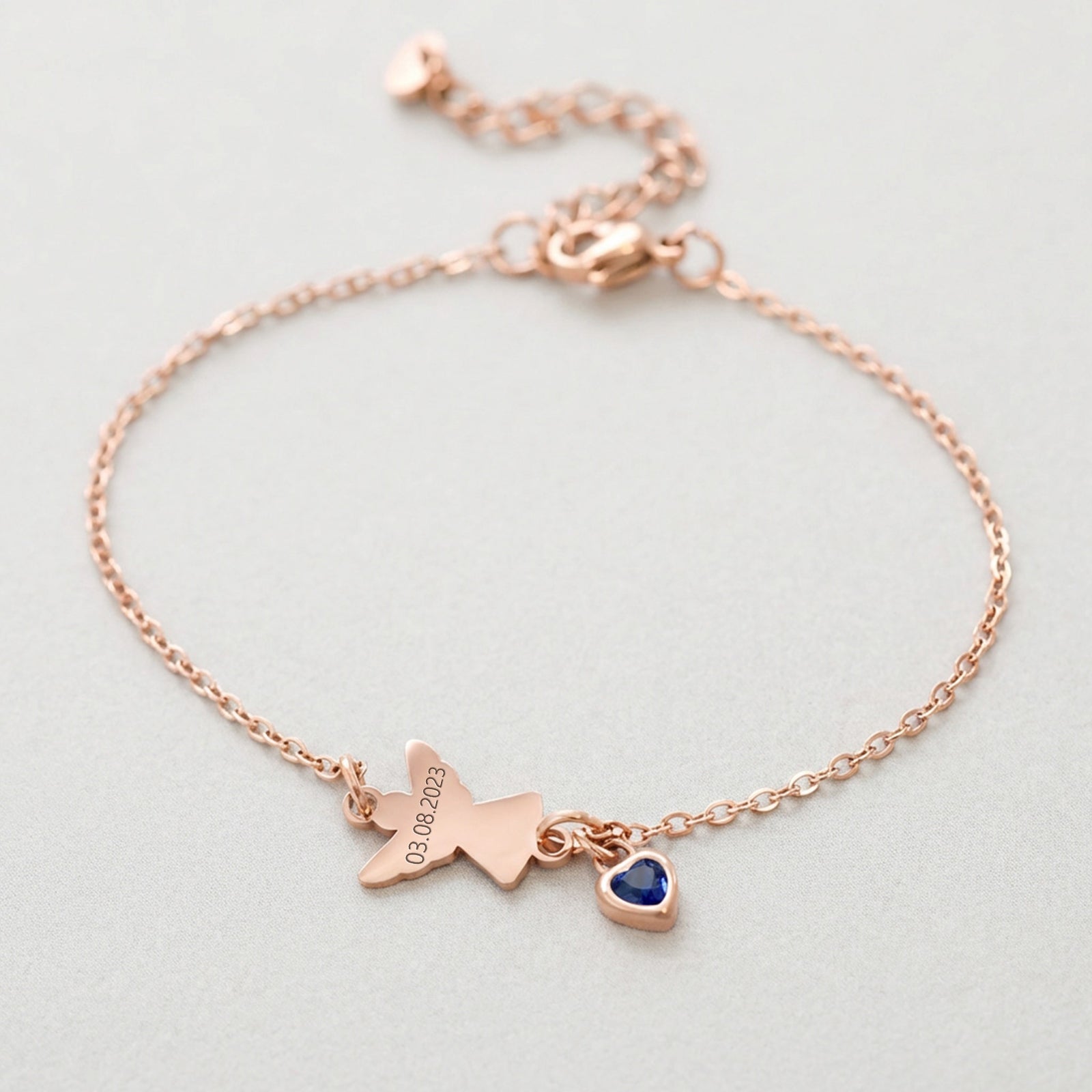 Engel Armband mit Zirkonia Geburtsstein in Roségold – Flatlay mit graviertem Datum und blauem Stein