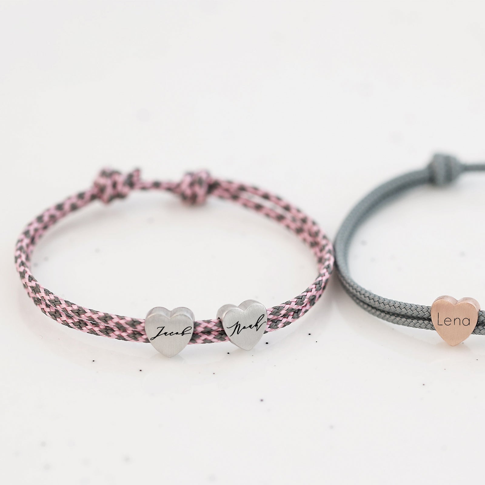 Zwei Herzarmbänder aus Segeltau – rosa-schwarz mit Silberherzen 'Zeek' und 'Noah', grau mit Roségold-Herz 'Lena'