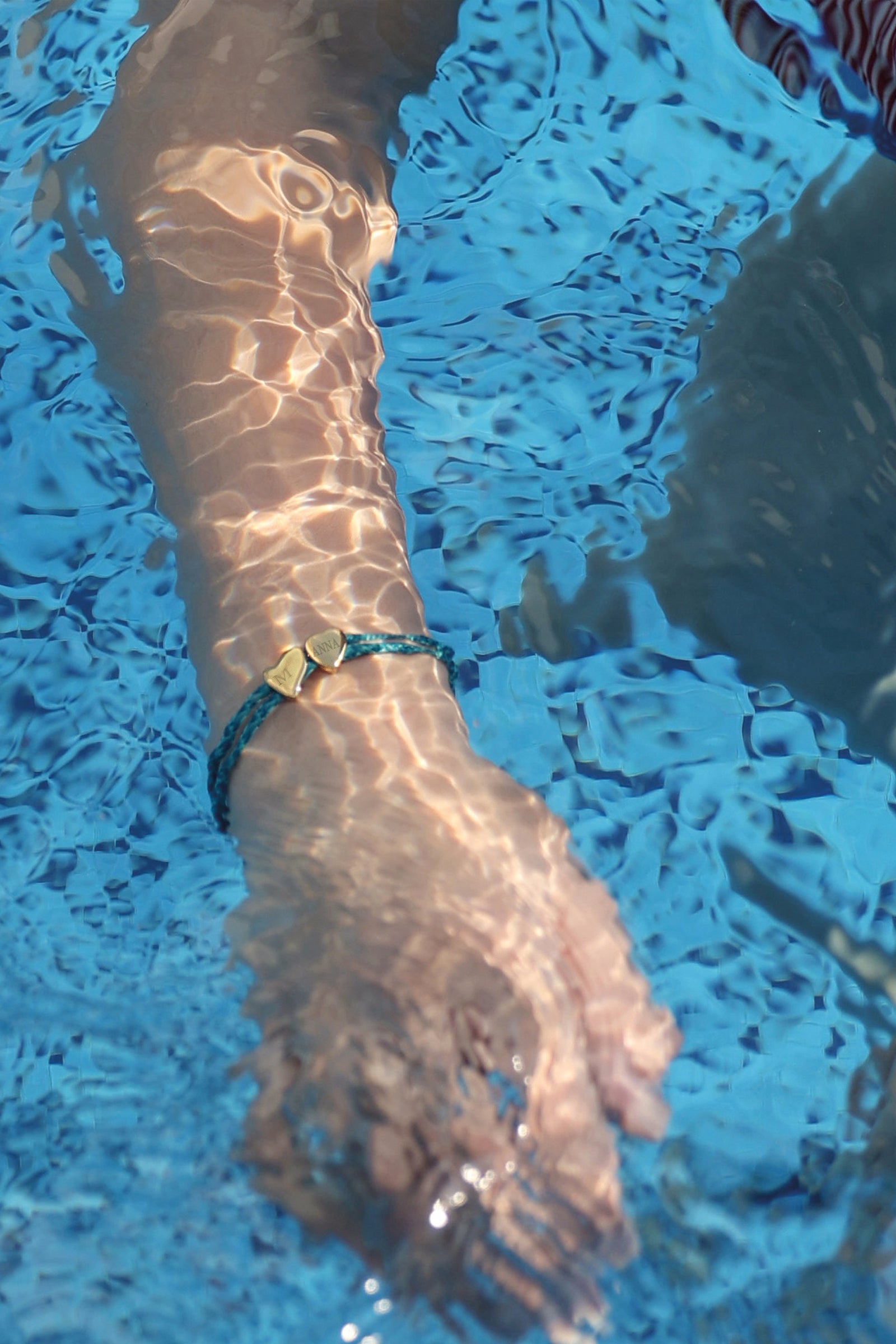 Herzarmband aus Segeltau in Türkis mit zwei goldenen Herzen – Frau trägt es beim Schwimmen im Pool