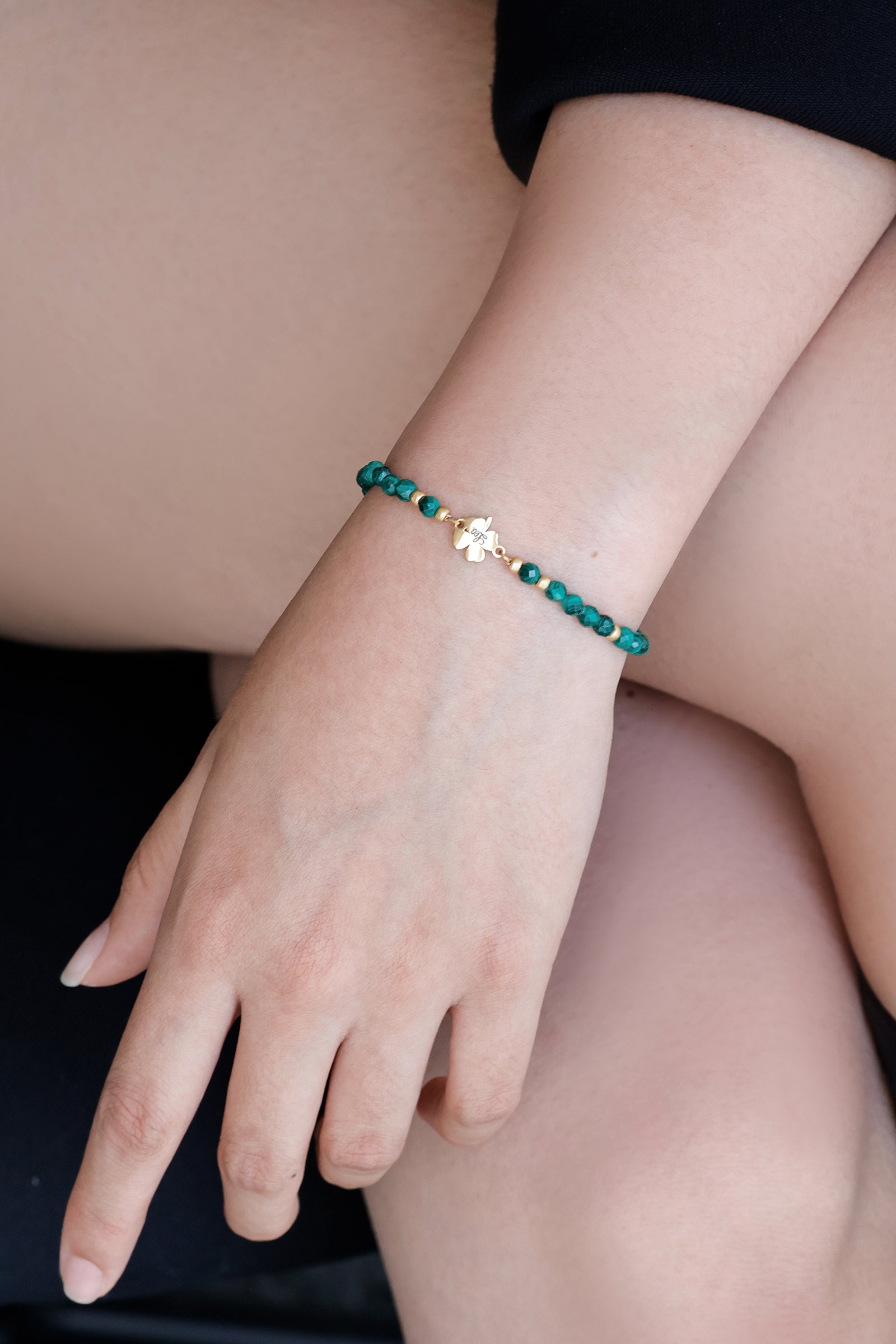 Frau trägt Malachit-Armband mit Kleeblatt in Silber, sitzend mit Blick auf das Handgelenk
